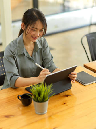 Cropped shot of smiling female office worker working with digital tablet on wooden desk in modern office roomの写真素材