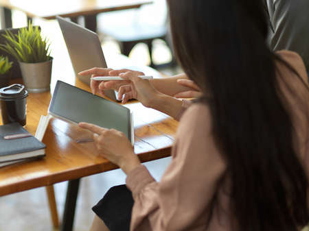 Cropped shot of female office worker using digital tablet and talking with her colleague in meeting...