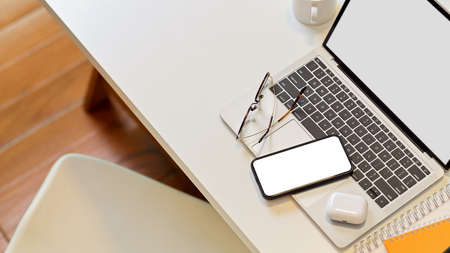 Top view of worktable with smartphone, laptop, eyeglasses, supplies and copy space with white chair in office room, clipping pathの写真素材