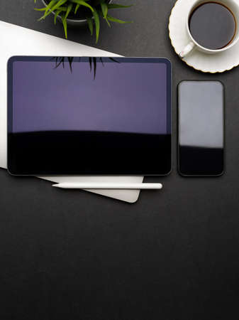 Top view of dark creative flat lay workspace with digital tablet, smartphone, laptop, coffee cup and...