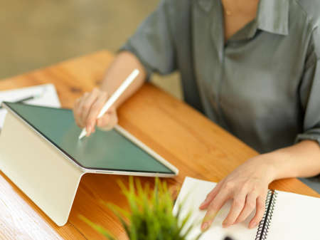 Top view of female worker hands working with mock up digital tablet and stationery on wooden tableの写真素材