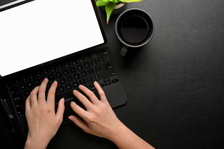 Top view of female hands typing on tablet keyboard on black table with cup and copy space, clipping pathの写真素材