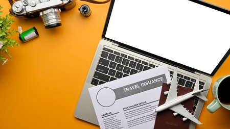 Top view of creative flat lay photo of yellow table with laptop, travel insurance form, passport, camera, and airplane model, clipping pathの写真素材