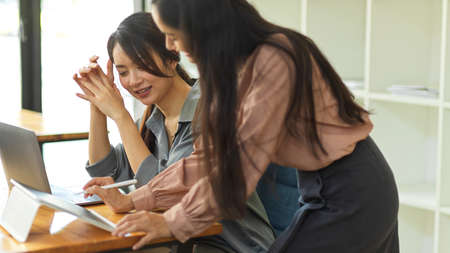 Portraits of two businesswomen sharing idea to each other while working together in office roomの写真素材