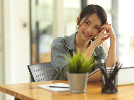 Half-length portrait of friendly businesswoman smiling to camera while relaxing at workplaceの写真素材