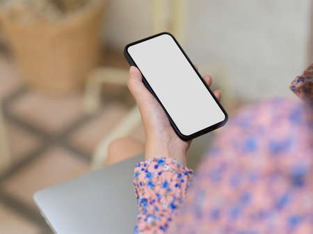 Close up view of female hand holding smartphone with mock up screen while relaxed sitting in cafe, clipping pathの写真素材