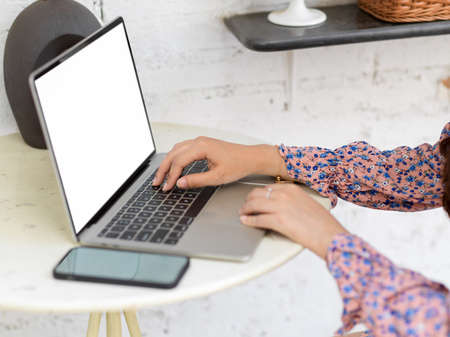 Side view of female hand working with laptop and smartphone on round table in living room, clipping pathの写真素材