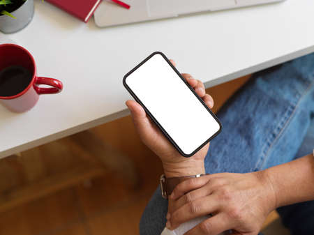 Top view of male hold smartphone with mock up screen in his hand while siting at workplaceの写真素材