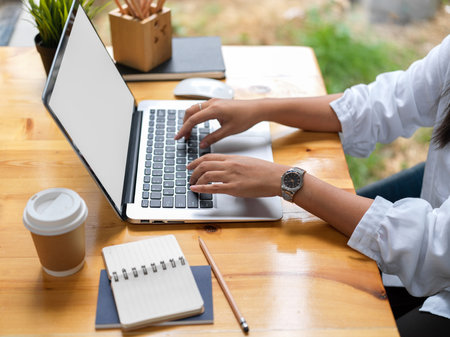 Side view of young businesswoman typing on laptop computer in modern office roomの写真素材