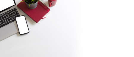 Creative flat lay workspace with smartphone, laptop, notebook and copy space on white background, top viewの写真素材