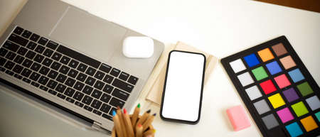 Top view of designer workspace with smartphone, laptop and paint tools on white table, clipping pathの写真素材