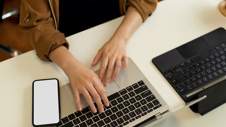 Top view of female hand typing on laptop keyboard with smartphone and another laptop on white desk, clipping pathの写真素材