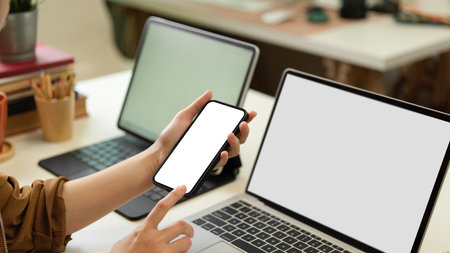 Close up view of female hands using smartphone while sitting office desk with two laptops, clipping pathの写真素材