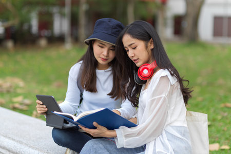 Side view of young pretty female university students outdoor study, tutoring to prepare for up coming their exam at park in universityの写真素材