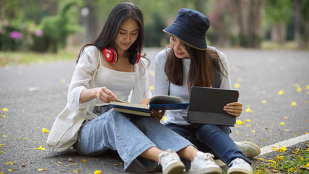 Portraits of young pretty female university students outdoor study with books and digital tablet while sitting on the ground in universityの写真素材