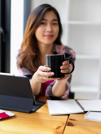 Cropped shot of female teenager holding coffee cup while relaxing at study tableの写真素材