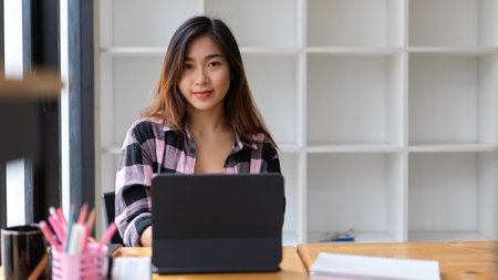 Portrait of young female student looking into camera while doing assignment in libraryの写真素材