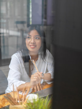 View through glass wall of female worker smiling and enjoying with the view out of workplace windowの写真素材