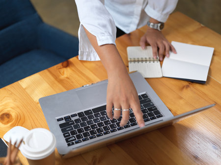 Top view of female using index finger pointing on laptop screen on wooden table with stationeryの写真素材