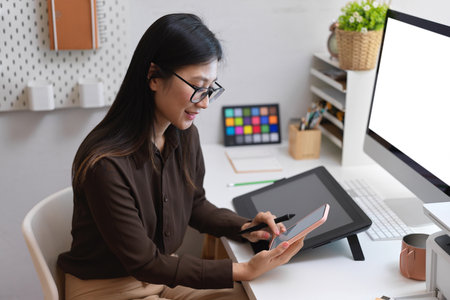 Side view of female office worker hand using smartphone while working with designer suppliesの写真素材