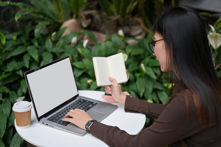 Side view of young female worker working with laptop and notebook on round table at cafeの写真素材