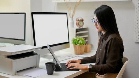 Side view of female office worker working with digital tablet on computer desk in office roomの写真素材