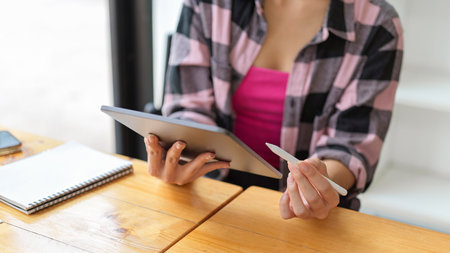 Close up view of young female hands using digital tablet while sitting at wooden table in cafeの写真素材