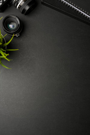 Top view of dark creative flat lay workspace with camera, lens, plant pot and copy space on black tableの写真素材