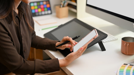 Side view of female graphic designer using smartphone while sitting at office deskの写真素材