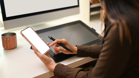 Cropped shot of female designer using smartphone while working at office desk, clipping pathの写真素材