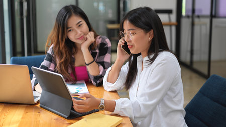 Portraits of two female students doing group assignment together and calling to another friend to consultの写真素材