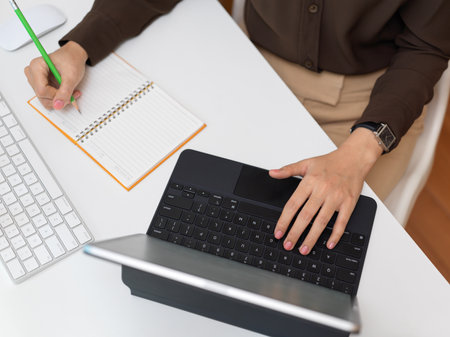 Top view of female office worker working with digital tablet and stationery on computer deskの写真素材