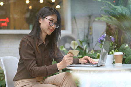 Side view of female office worker doing online banking on laptop while sitting in cafeの写真素材