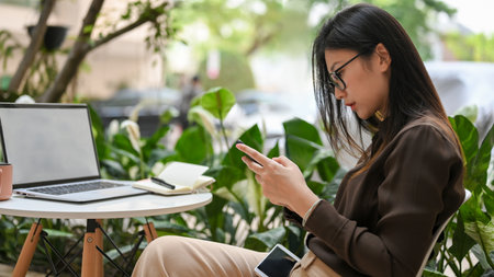 Side view of young female worker using smartphone while relaxed sitting in garden at officeの写真素材