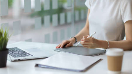 Close up view of female hands using digital tablet on the table with laptop and stationery in...
