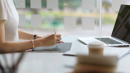 Side view of female student hand using digital tablet to do homework on white desk in libraryの写真素材