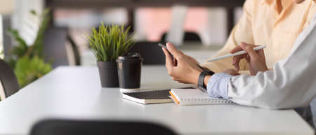 Side view of two office worker hands using digital tablet while discussing on their work in simple meeting roomの写真素材