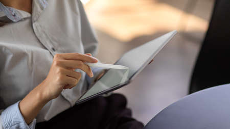 Close up view of young female using mock up blank screen digital tablet while sitting in office roomの写真素材
