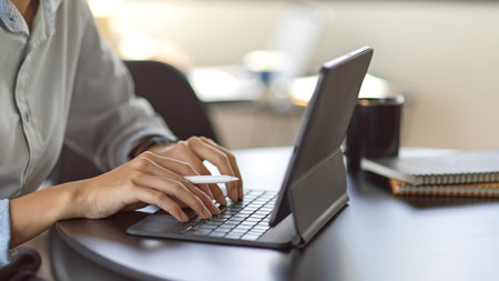 Cropped shot of young female typing on tablet keyboard in office roomの写真素材