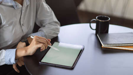 Cropped shot of woman using mock up Digital tablet in office room with coffee cup and paper on the deskの写真素材