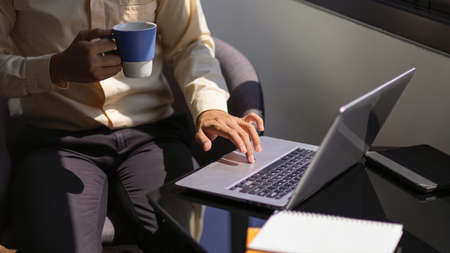 Cropped shot of businessman hand using laptop and holding coffee cup while working at portable workspaceの写真素材