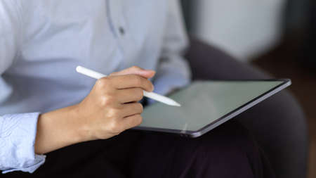 Cropped shot young businesswoman writing on digital tablet while sitting in the office roomの写真素材