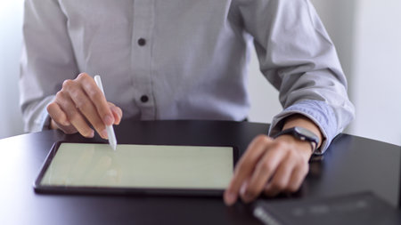 Close up view of businessperson hand with stylus pen touching on mock-up tablet screen on round tableの写真素材