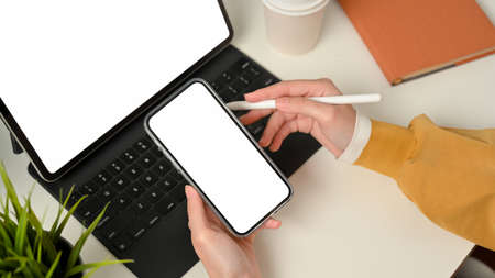 Top view of female hands working with smartphone and digital tablet include clipping path screen on white deskの写真素材