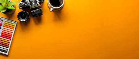 Yellow creative flat lay workspace with oil pastels, camera, coffee mug and copy space, top viewの写真素材