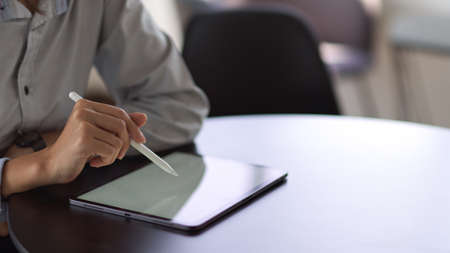 Cropped shot of businessperson hand with stylus pen touching on mock-up tablet screen on round tableの写真素材