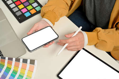 Cropped shot of female designer hands working with smartphone on office desk with tablet and designer supplies, clipping pathの写真素材