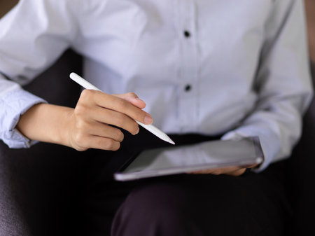 Cropped shot of businessperson hand with stylus pen touching on digital tablet screen on black tableの写真素材