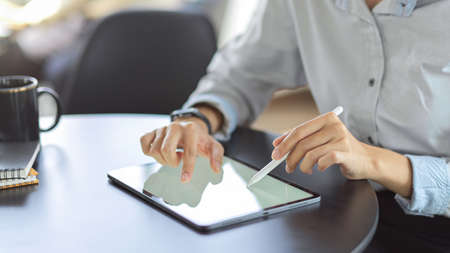 Close up view of young female using mock up blank screen digital tablet while working on her projectの写真素材