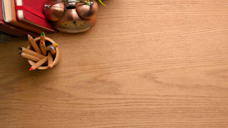 Overhead shot of simple workspace with colour pencils, clock books and copy space on wooden tableの写真素材